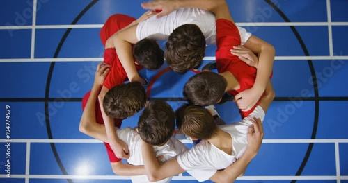 4K Overhead view looking down, young boys standing in a circle on basketball court go into huddle before a game