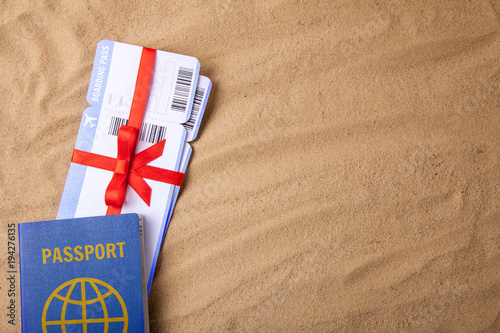 Air tickets as a gift with a red ribbon and bow. Passport with visas. Background sand beach. Copy space for text