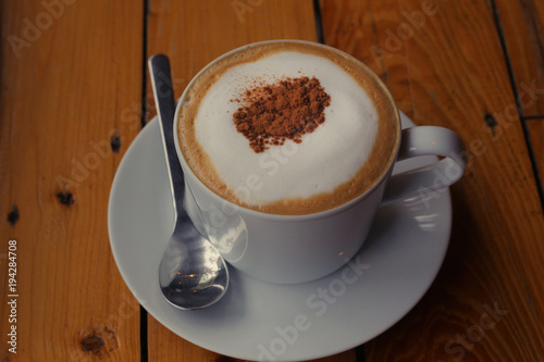 cappuchino coffee in white porcellan cup and saucer with spoon and cinnamon close photo