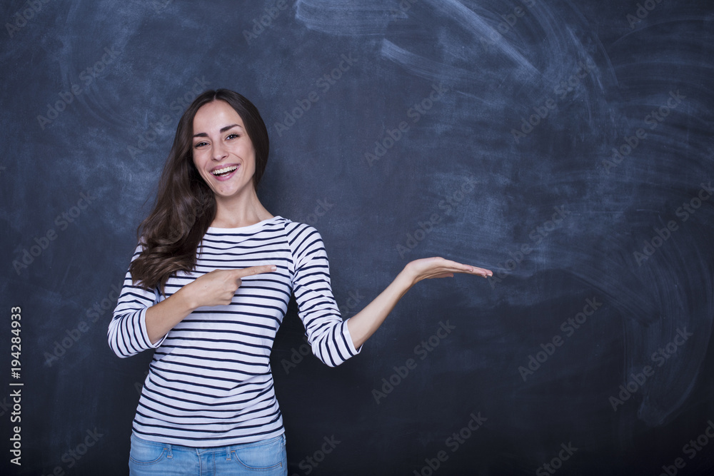 Happy smiling young business woman pointing to empty chalkboard with copy space