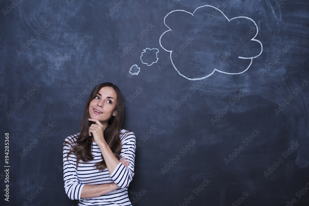 Where to go for the weekend? Attractive young woman in casual clothes standing and dreaming at the blackboard Where to go for the weekend? Attractive young woman in casual clothes standing and dreaming at the blackboard