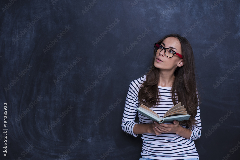 Study concept. Beautiful smiling woman with book on blackboard background Study concept. Beautiful smiling woman with book on blackboard background