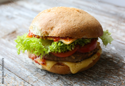 Tasty homemade cheeseburger with mustard, tomatoes and green lettuce. Sesame burgers on wooden background. Food photo.
