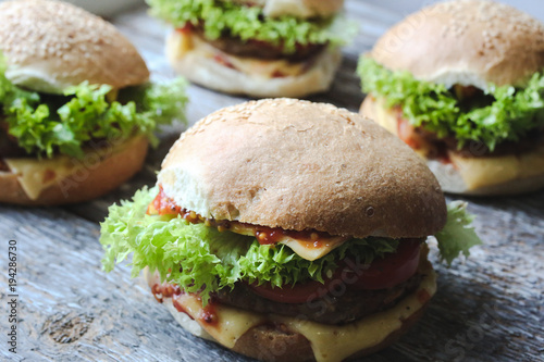 Tasty homemade cheeseburger with mustard, tomatoes and green lettuce. Sesame burgers on wooden background. Food photo.