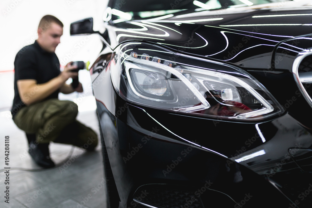 Fototapeta premium Car detailing - Worker with orbital polisher in auto repair shop. Selective focus.