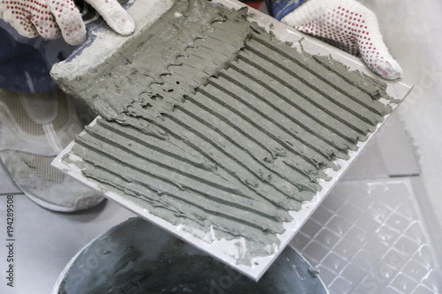Repair - interior decoration. Laying of floor ceramic tiles. Men's hands tiler in gloves with  spatula spread  cement mortar on  ceramic floor tile.