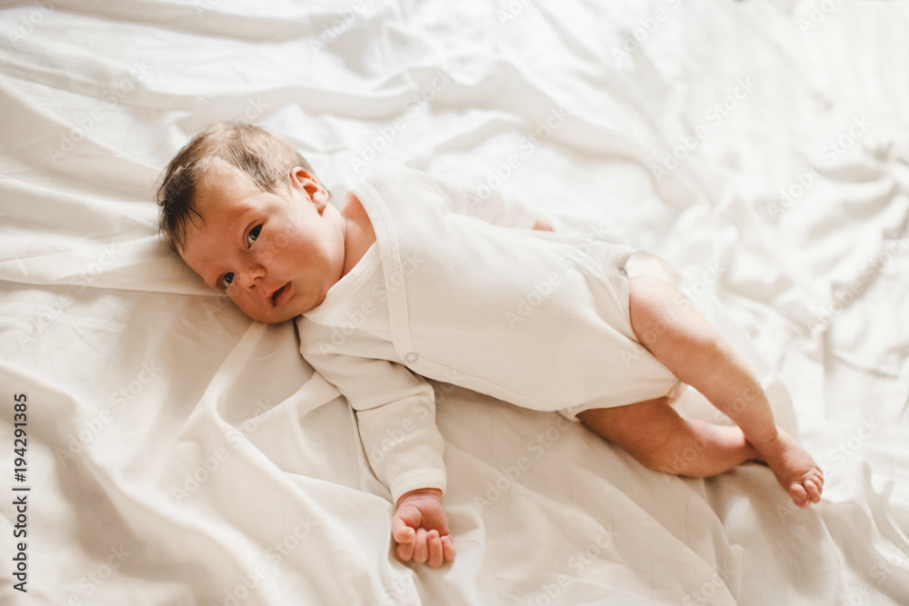 Newborn baby lies on white bed in a bright room Newborn baby lies on white bed in a bright room