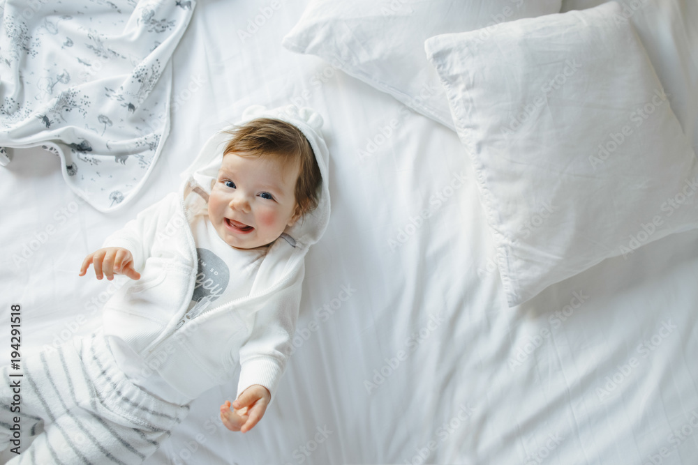 Little baby-girl dressed in casual-style lies on white bed