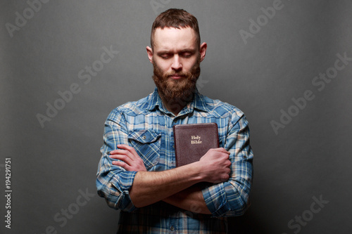 Tableau sur toile Handsone man reading and praying over Bible in a dark room over gray texture
