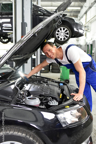 freundlicher KFZ Mechaniker untersucht Motor eines Autos in einer Werkstatt // friendly car repair men check the engine in car workshop