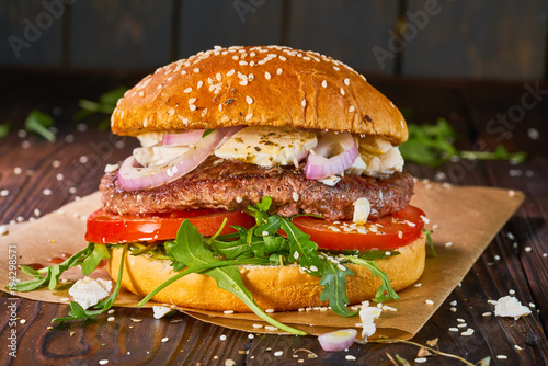 Home made beef burger with arugula and tomatoes served on wooden background