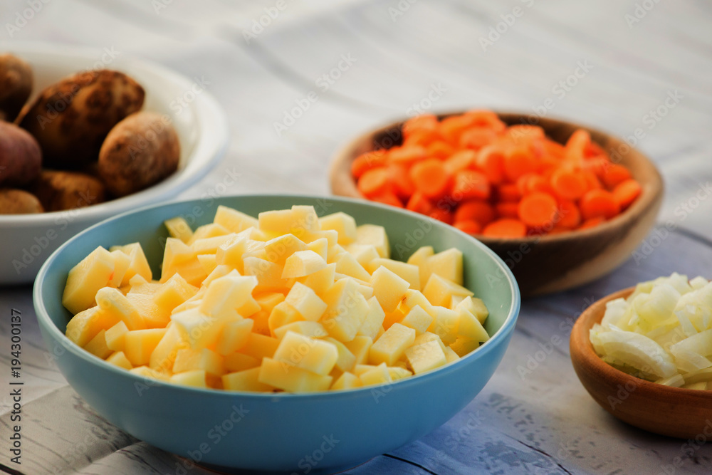 Bowls with chopped fresh and raw vegetables in small pieces prepared for veggie soup cooking