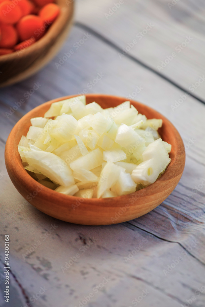 Chopped fresh and raw white onion slices in wooden bowl with bulbs