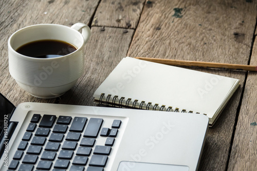 Top view of blank notebook with white coffee  laptop and with natural light on wooden table.