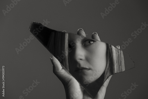 Fotografie, Obraz Woman looking at her face in a shard of broken mirror artistic conversion