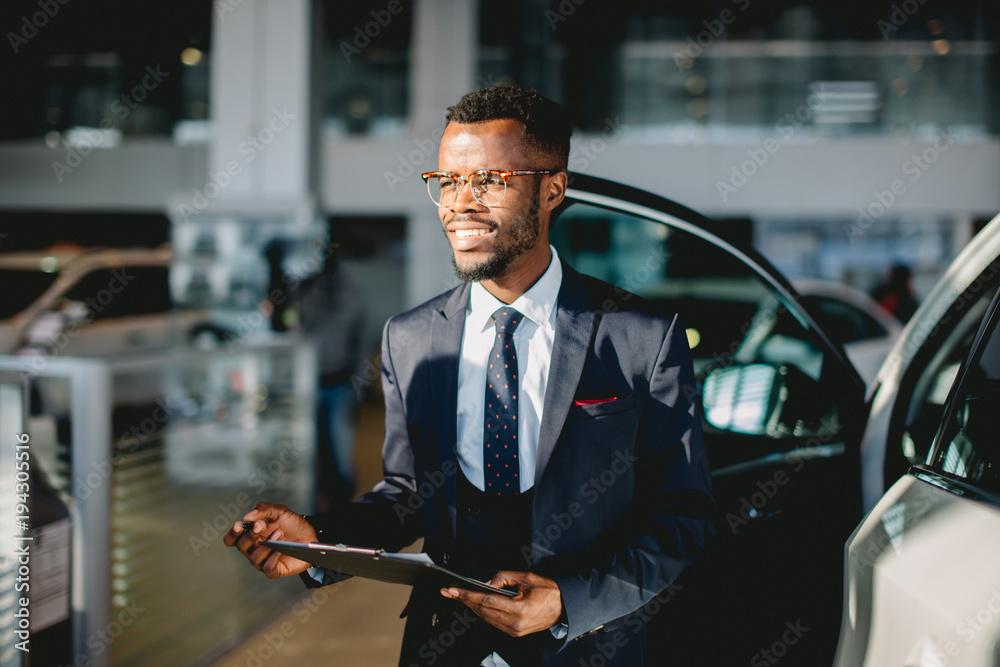 Handsome young african car salesman standing at the dealership holding a tablet