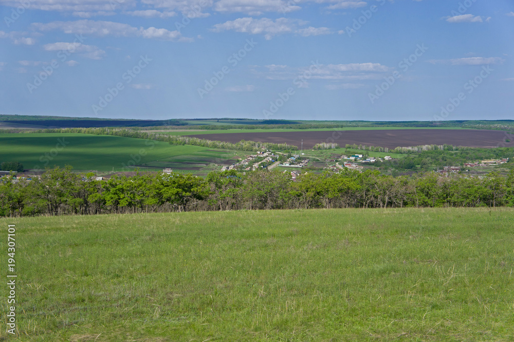 Bright spring greens and a blue sky over a distant village. Green meadow and plowed land in the background. Bright spring greens and a blue sky over a distant village. Green meadow and plowed land in the background.