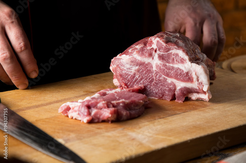 Cook cuts raw meat on a wooden cutting board