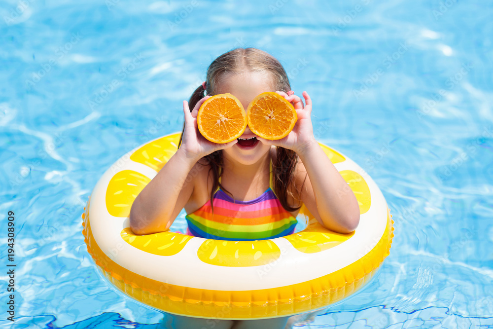 Child in swimming pool. Kid eating orange. - obrazy, fototapety, plakaty 