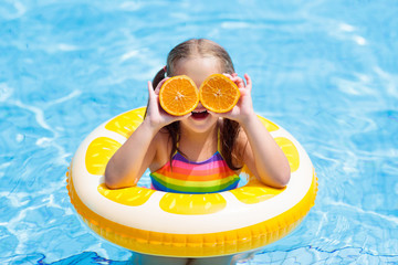 Child in swimming pool. Kid eating orange.