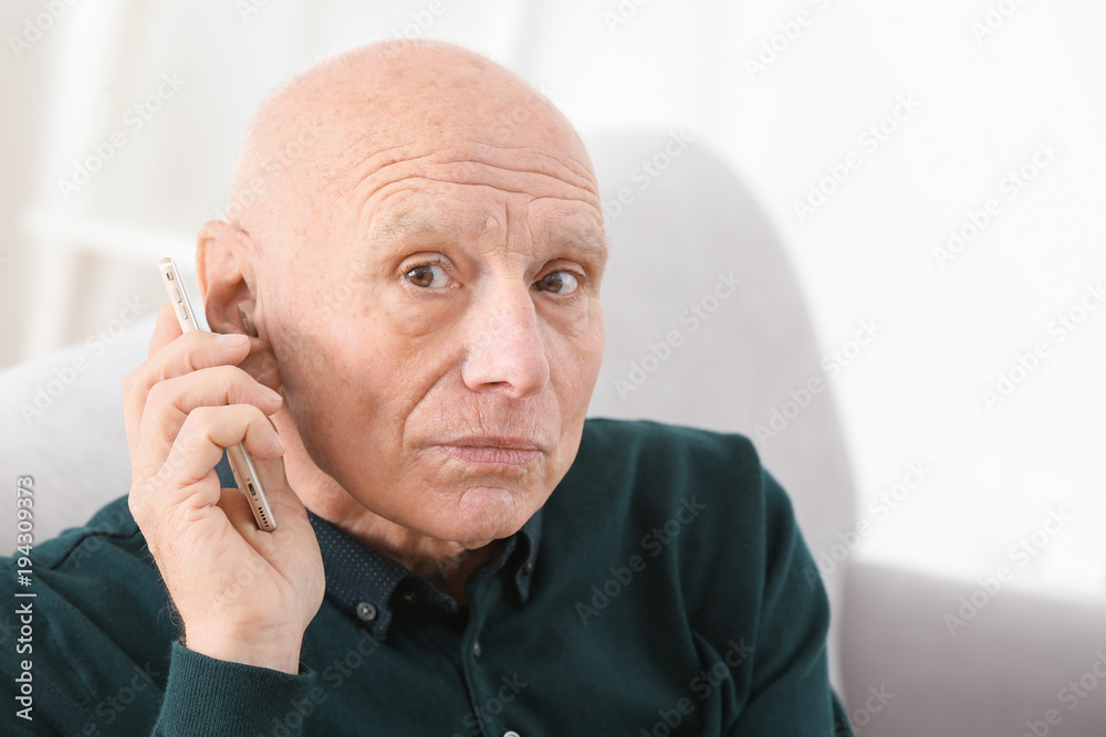 Senior man with hearing aid talking on phone indoors Senior man with hearing aid talking on phone indoors