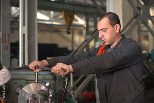 metalworking industry: factory man worker in uniform working on lathe machine in workshop photo