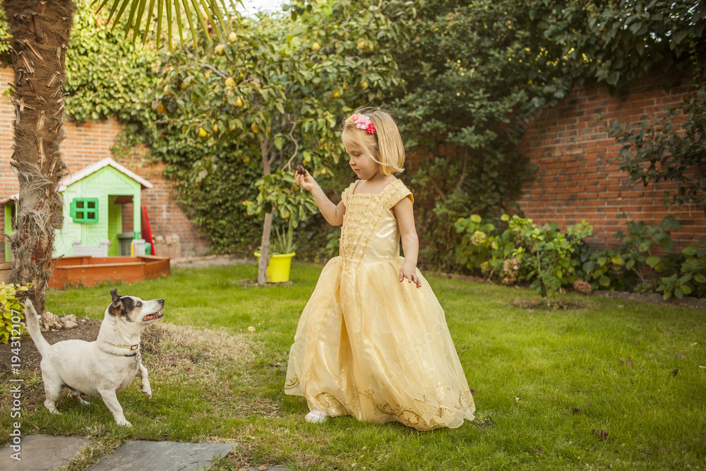Kid dress up as a princess playing with a dog. Outdoors.
