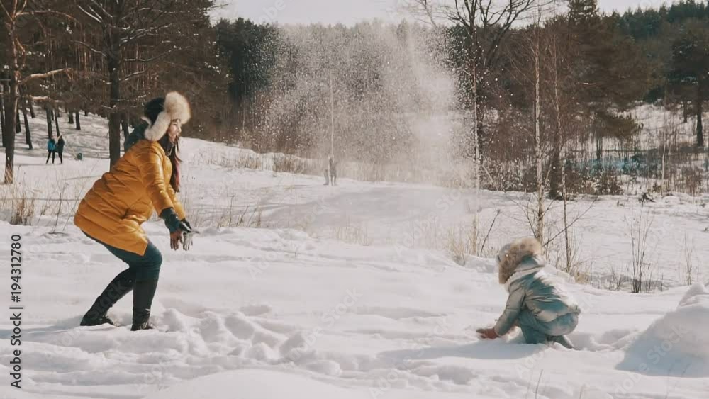 Mother playing snow with little daughter in slow motion. Happy winter rest. Family have fun in sunny winter day outdoors
