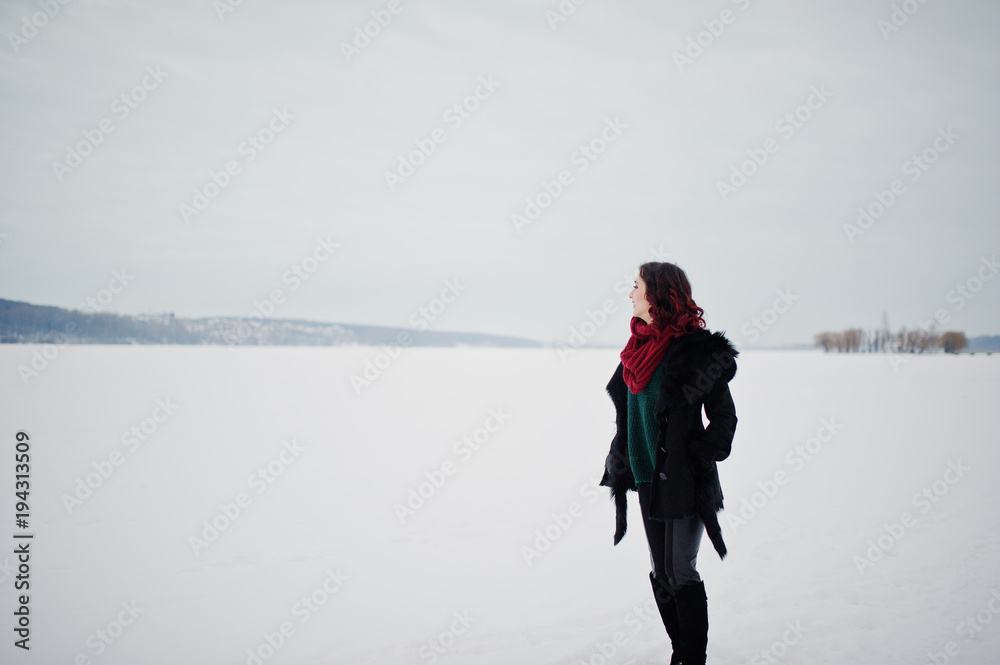 Brunette girl in green sweater and red scarf outdoor frozen lake on evening winter day.