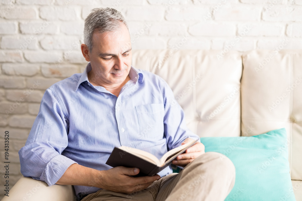 Middle aged man reading his favorite novel at home