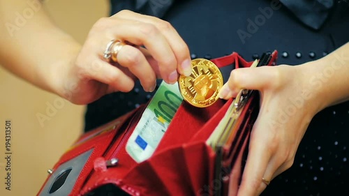 SLOW MOTION: girl holds a red wallet in her hand and places a gold Bitcoin in a wallet.