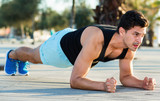 Strong sporty man doing press exercises holding plank outdoors