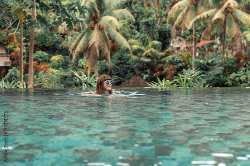 Happy young woman in a tropical infinity pool. Luxury resort on Bali island.