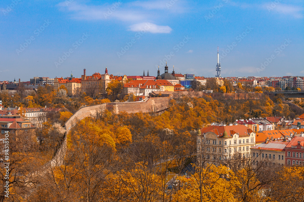 Prague skyline with wall, castle and living blocks red rooftops with park and trees. Fall season