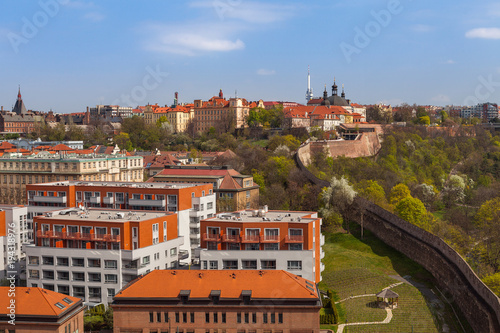 Prague skyline with wall, castle and living blocks red rooftops with park and trees
