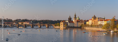 Boats floating by the Vltava river. Sunset over Charles Bridge and old town of Prague, Czech Republic. Wide panoramic view.