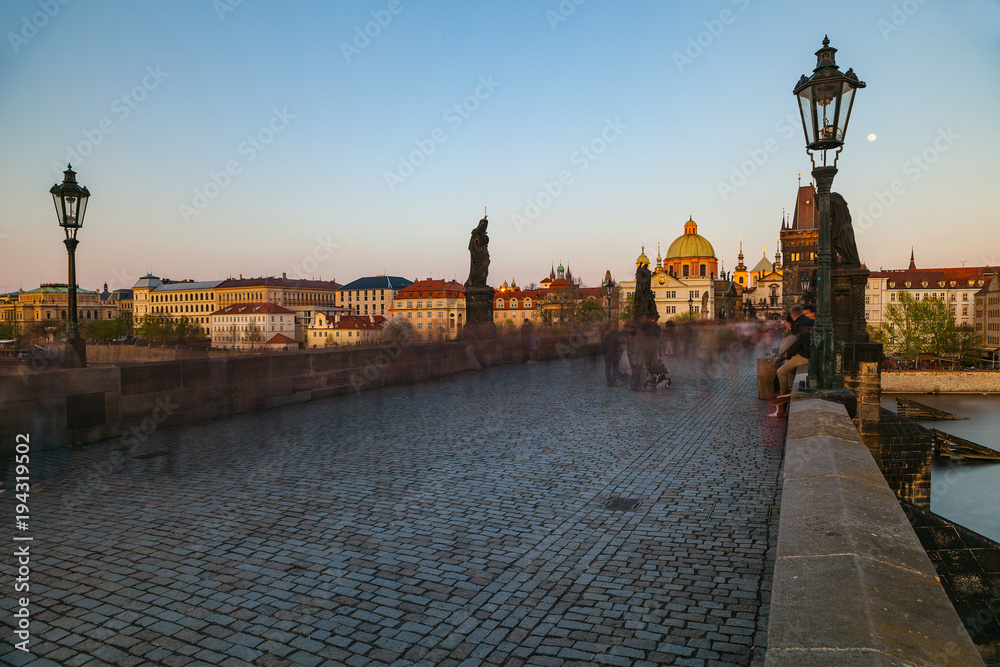Charles bridge at sunset. Motion blurred walking people shot with long exposure. Magical summer moments.
