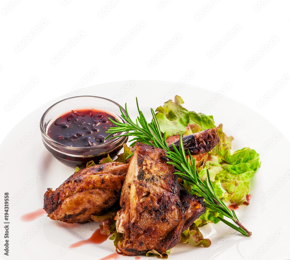 Fried pork ribs with seasonings greens and berry sauce on a white plate. Clipping path of the plate. Fried pork ribs with seasonings greens and berry sauce on a white plate. Clipping path of the plate.