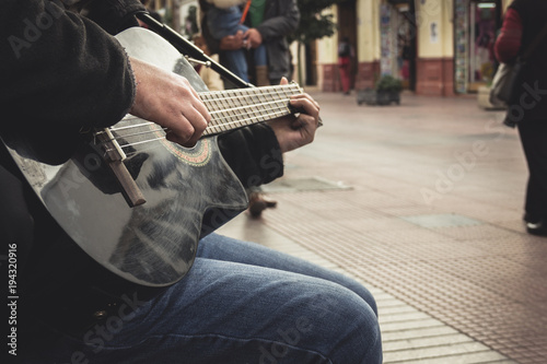 Hands of young man playing black guitar on the street as pedestrians pass by in La Serena downtown, Chile