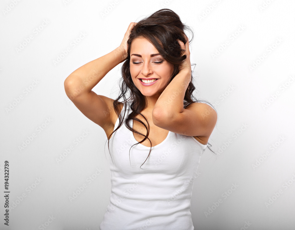Beautiful positive excited laughing young woman holding the hands the hair on the head in white shirt and with toothy smile and close eyes on white background Beautiful positive excited laughing young woman holding the hands the hair on the head in white shirt and with toothy smile and close eyes on white background