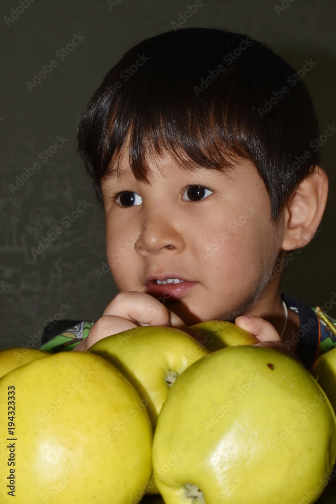 The little boy brown-eyed brunette sits at a table with apples, is going to eat and dreams The little boy brown-eyed brunette sits at a table with apples, is going to eat and dreams