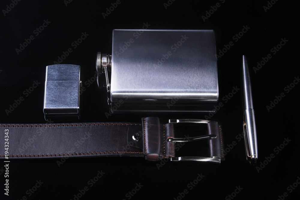 Stainless hip flask, lighter, pen and luxury belt isolated on mirror black background. Stainless hip flask, lighter, pen and luxury belt isolated on mirror black background.