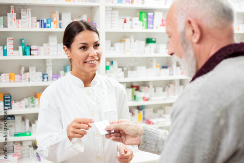 Beautiful young pharmacist selling medications to senior patient photo