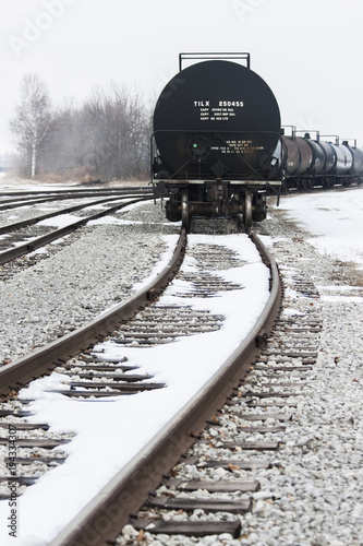 Tanker Train Cars on the right side of several sets of tracks, in the fog with snow on the ground.