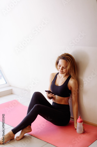 girl using smartphone and resting on wooden floor after exercises