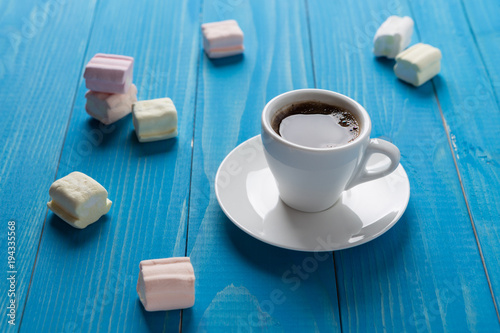 a cup of black coffee on blue boards surrounded by scattered marshmallows