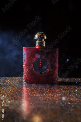 Wet red bottle of perfume on dark background