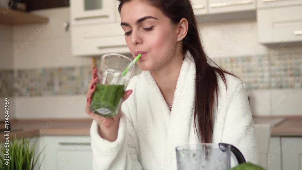 Beautiful brunette enjoying a glass of green smoozie at the kitchen table, concept of healthy lifestyle, peaceful morning time Beautiful brunette enjoying a glass of green smoozie at the kitchen table, concept of healthy lifestyle, peaceful morning time