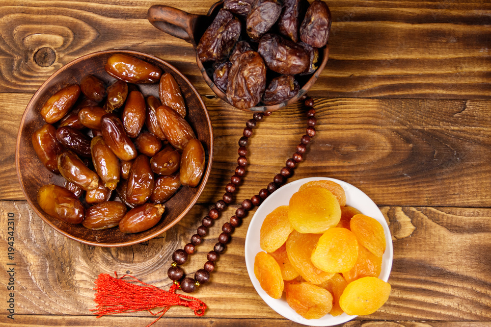 Dried apricots and dates fruit with wooden rosary on wooden table. Top view