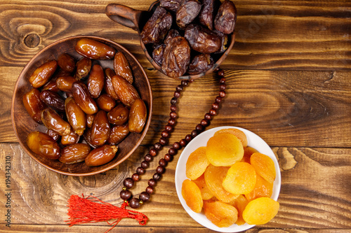 Dried apricots and dates fruit with wooden rosary on wooden table. Top view